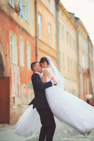 Elegante noivo levantando sua bela noiva morena no fundo da parede branca velha — Fotografia de Stock