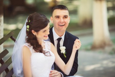 Gelin ve damat bankta parlak giysiler içinde.