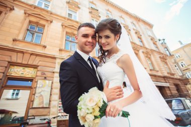 Fotoğraf çekim düğün. Gelin ve damat şehirde yürüyüş. Kucaklayan ve birbirine bakarak evli çift. Buket tutarak. Açık, tam vücut