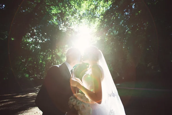 Pareja joven besándose en vestido de novia. Novia sosteniendo ramo de flores —  Fotos de Stock