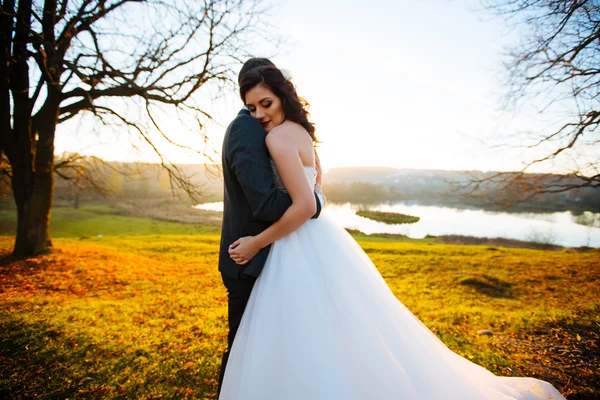 Gelukkig lachend jonggehuwden buiten wandelen, kussen en omhelzen op hun trouwdag — Stockfoto