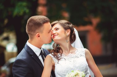 Fotoğraf çekim düğün. Gelin ve damat şehirde yürüyüş. Kucaklayan ve birbirine bakarak evli çift. Buket tutarak. Açık, tam vücut