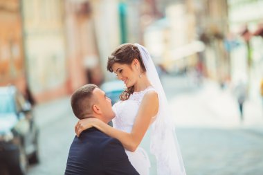 Damat nazik hareket ettirildiğinde gelin, onu tutarak onun kollarında ve tutkuyla öper, düğün fotoğraf güneşli bir kum renkli duvarlar arka plan üzerinde. Yeni evli çift Park, sokak tango dans.