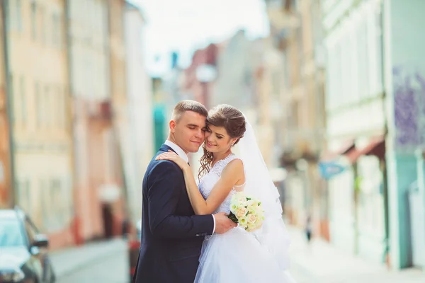 Esküvői fotó lövés. Menyasszony és a vőlegény, séta a városban. A házaspár átfogó és néztek egymásra. Gazdaság csokor. Kültéri, teljes test — Stock Fotó