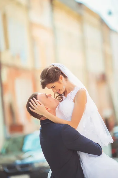 Ήπια κλίση νύφη γαμπρός, κρατώντας το στην αγκαλιά του και με πάθος φιλιά, φωτογραφία γάμου, μια ηλιόλουστη μέρα σε φόντο της άμμου-χρώματα στους τοίχους. Νιόπαντρο ζευγάρι που χορεύει στο πάρκο, Οδός τανγκό. — Φωτογραφία Αρχείου