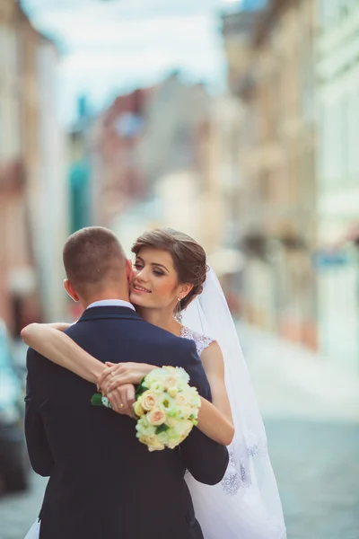 Hochzeitsfotoshooting. Braut und Bräutigam beim Gang durch die Stadt. Eheleute, die sich umarmen und anschauen. Blumenstrauß halten. draussen, ganzkörper — Stockfoto