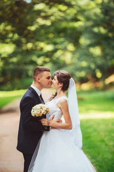 Giovane coppia che si bacia in abito da sposa. Sposa che tiene mazzo di fiori — Foto Stock