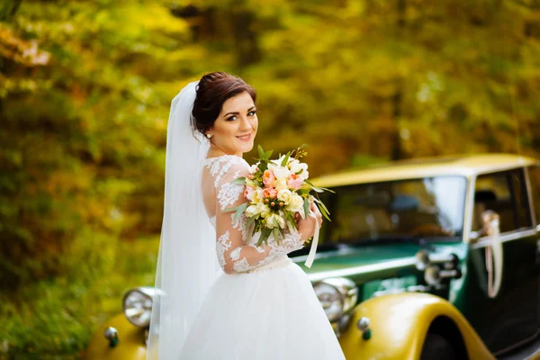 Gelukkige bruid met boeket in de buurt van bruiloft auto met bloemen — Stockfoto