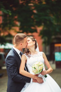 Fotoğraf çekim düğün. Gelin ve damat şehirde yürüyüş. Kucaklayan ve birbirine bakarak evli çift. Buket tutarak. Açık, tam vücut