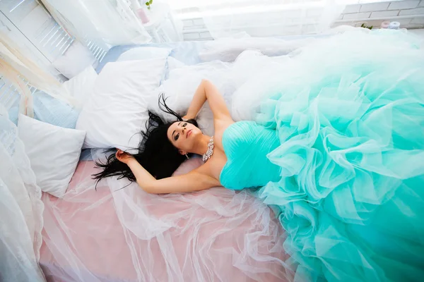 Bella giovane donna sdraiata su un letto in un vestito, sguardo pensieroso — Foto Stock