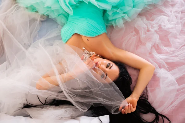 Vacker ung kvinna i en grön klänning med lockigt långt hår, ligger på sängen — Stockfoto