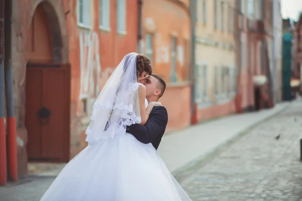 Fotografia de casamento. Noiva e noivo andando na cidade. Casamento casal abraçando e olhando um para o outro. A segurar o buquê. Ao ar livre, corpo inteiro — Fotografia de Stock