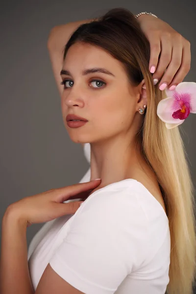 Schoonheidsportret. Mooi stijlvol meisje met orchidee bloem. Een perfecte gezichtshuid. Gezond haar. — Stockfoto