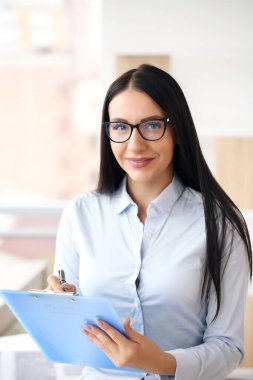 Gözlüklü, iş yerinde oturan gülümseyen genç bir iş kadınının portresi.