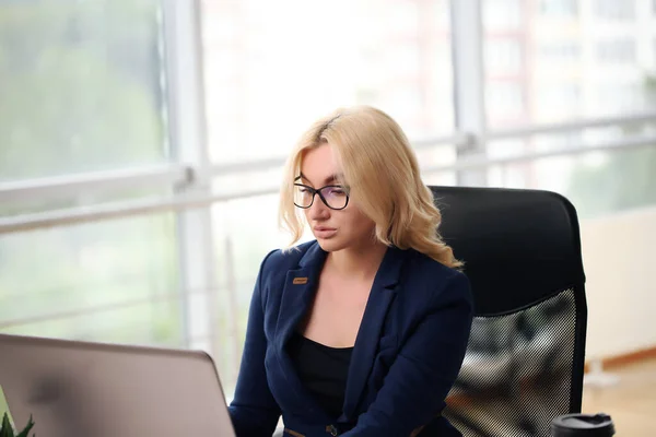 Photo of serious manager or director woman wearing formal clothing and eyeglasses holding in hands paper documents while working in office on laptop