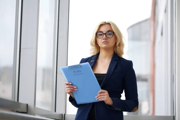 Zdjęcie poważnej kierowniczki lub reżyserki noszącej formalną odzież i okulary trzymające w ręku dokumenty papierowe podczas pracy w biurze na laptopie — Zdjęcie stockowe