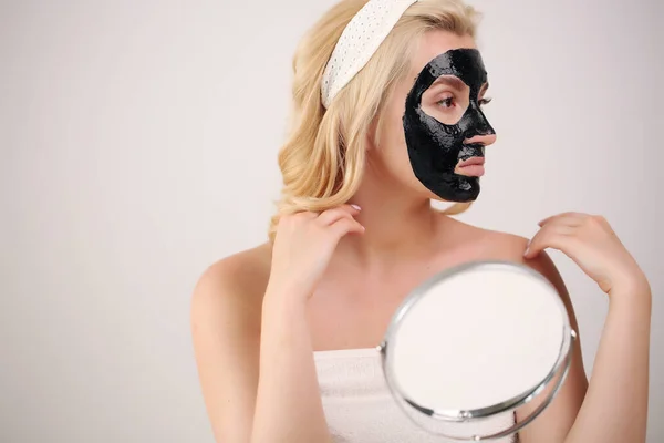 Beautiful woman with black cleaning black charcoal mask on her face. Skin care, acne treatment, skin cleansing.