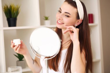 Evde oturuyor, aynaya bakıyor, gülüyor ve eğleniyor. Sabah cilt bakım rejimi.