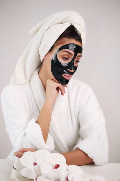 머리에 수건을 얹은 행복 한 여인이 얼굴 피부를 깨끗하게 하는 마스크를 쓴다 — 스톡 사진