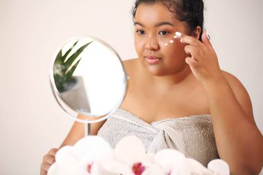 Çekici bir genç kadının yüzüne krem sürerken yakın plan portresi.