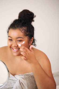 Güzel, genç Afrikalı Amerikalı kadın cildine krem sürüyor.