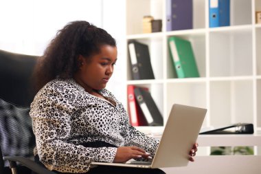 Afro iş kadını pencerede oturan ve ofisteki bilgisayarı kullanan gömlekli kadın..