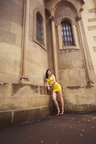 Beautiful girl in a yellow dress leaned on old architectural bui — Stock Photo, Image