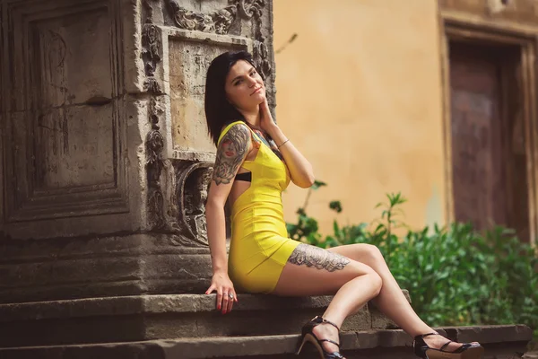 Красивая женщина в желтом платье, татуировки, сидит на архите — стоковое фото