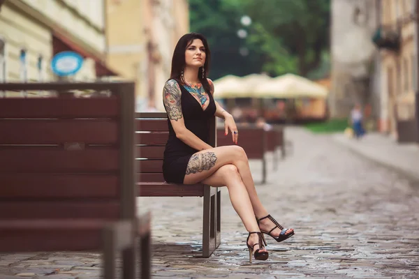 Beautiful girl in a black dress sitting on a bench, covered in t — Stock Photo, Image