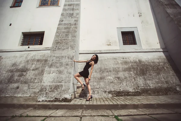 Красивая девушка в черном платье стоит рядом с архитектурными сооружениями — стоковое фото