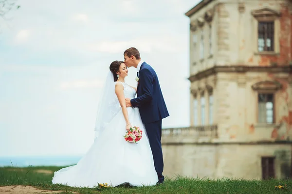 Blonde bride and brunette groom walking near old castle — Stock Photo, Image