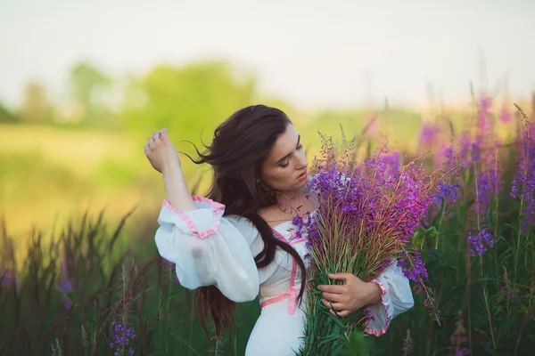 Menina em um vestido branco longo, acariciando o cabelo longo, de pé em uma fi — Fotografia de Stock