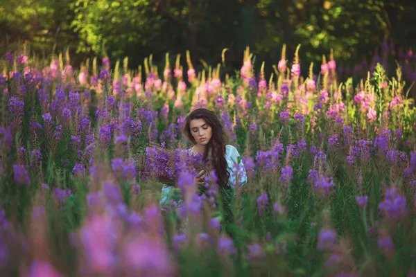 Jovencita en un campo de lavanda, sosteniendo flores en sus manos — Foto de Stock