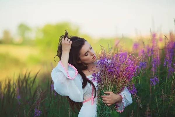 Ragazza in un abito lungo bianco, accarezzando i capelli lunghi, in piedi in un fi — Foto Stock