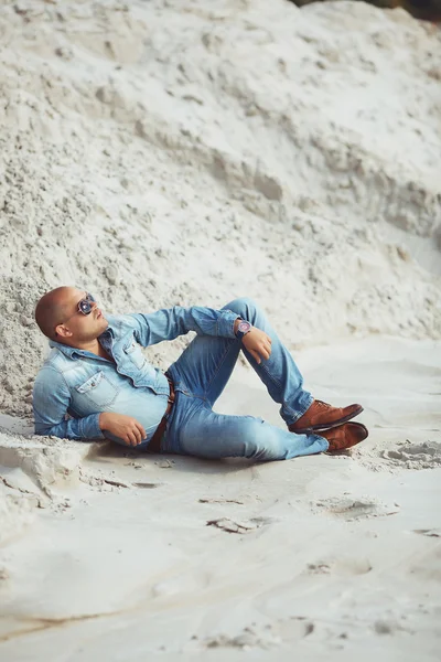 Joven en gafas se encuentra en la ropa vaqueros en la arena en Dubai — Foto de Stock