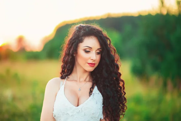 Bela jovem em um campo em vestido branco e tem blac longo — Fotografia de Stock