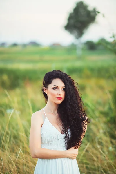 Bela jovem em um campo em vestido branco tem lindo lon — Fotografia de Stock