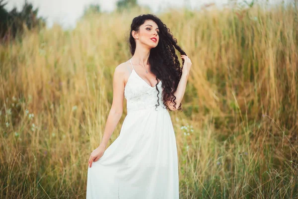 Bela jovem em um campo em vestido branco tem lindo lon — Fotografia de Stock
