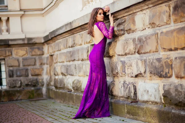 Beautiful girl in the purple dress leaned on the wall — Stock Photo, Image