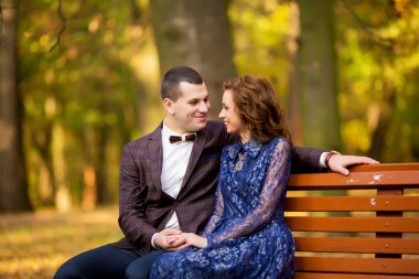 Groom and Bride sitting on bench in a park. wedding dress.