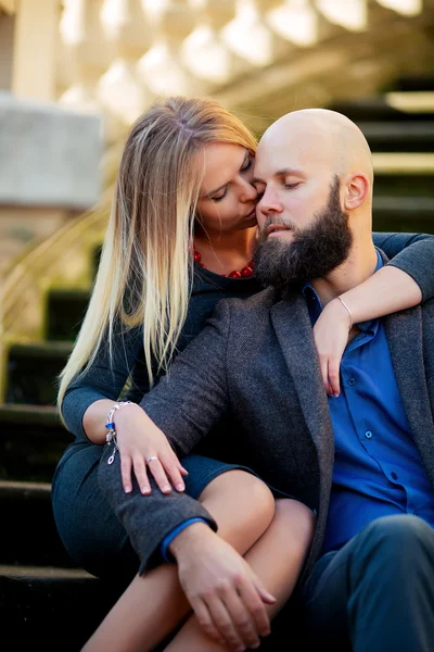 Young couple eyes closed, stylishly dressed, sitting on the steps, against a historic building — Stock Photo, Image