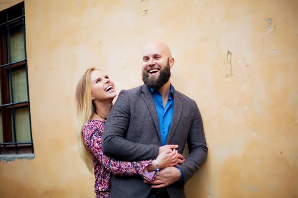 Feliz casal sorrindo, de pé perto da parede nos braços — Fotografia de Stock