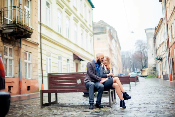 Los amantes de la ciudad de otoño sentados en un banco en el amor, abrazan tiernamente —  Fotos de Stock