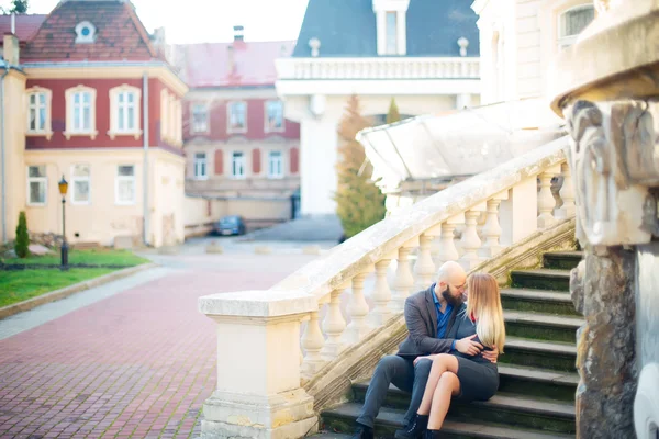 Одна красивая стильная пара молодая женщина и пожилой мужчина с длинной черной бородой сидя обнимая друг друга на открытом воздухе на осенней улице на лестнице солнечный день, горизонтальная картина — стоковое фото