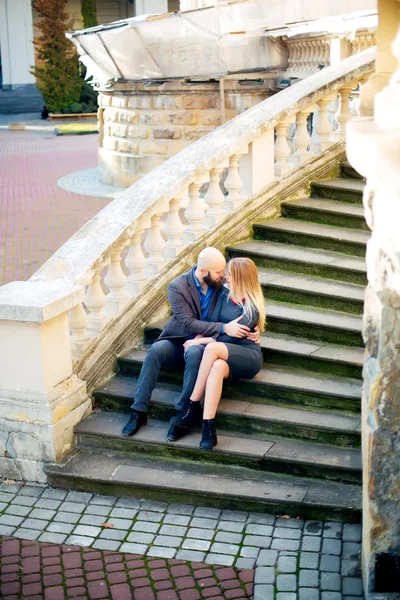 One beautiful stylish couple of young woman and senior man with long black beard sitting embracing close to each other outdoor in autumn street on stairs sunny day, horizontal picture — Stock Photo, Image