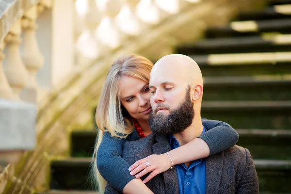 A young couple in love, stylishly dressed, sitting on the steps, against a historic building — Stock Photo, Image