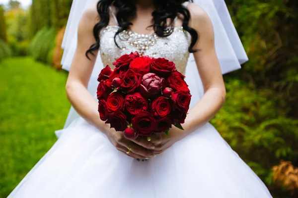 Bellissimo bouquet di colore bordeaux nelle mani della sposa in un abito bianco in piedi nel parco — Foto Stock