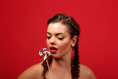 Güzellik moda modeli kız renkli lolipop yemek. Sürpriz komik genç kadınla saç modeli, çivi ve makyaj bej, kırmızı bir arka plan üzerinde izole örgü