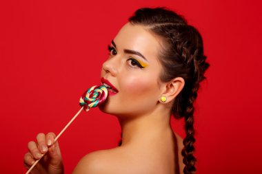 beautiful young woman licks candy with beautiful make-up isolated on a red background, beautiful hair braids