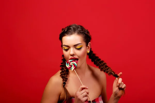 Studio close colorful portrait of a young sexy funny crazy fashion girl posing on a red background wall in style year dress with a pink lollipop. — Stock Photo, Image